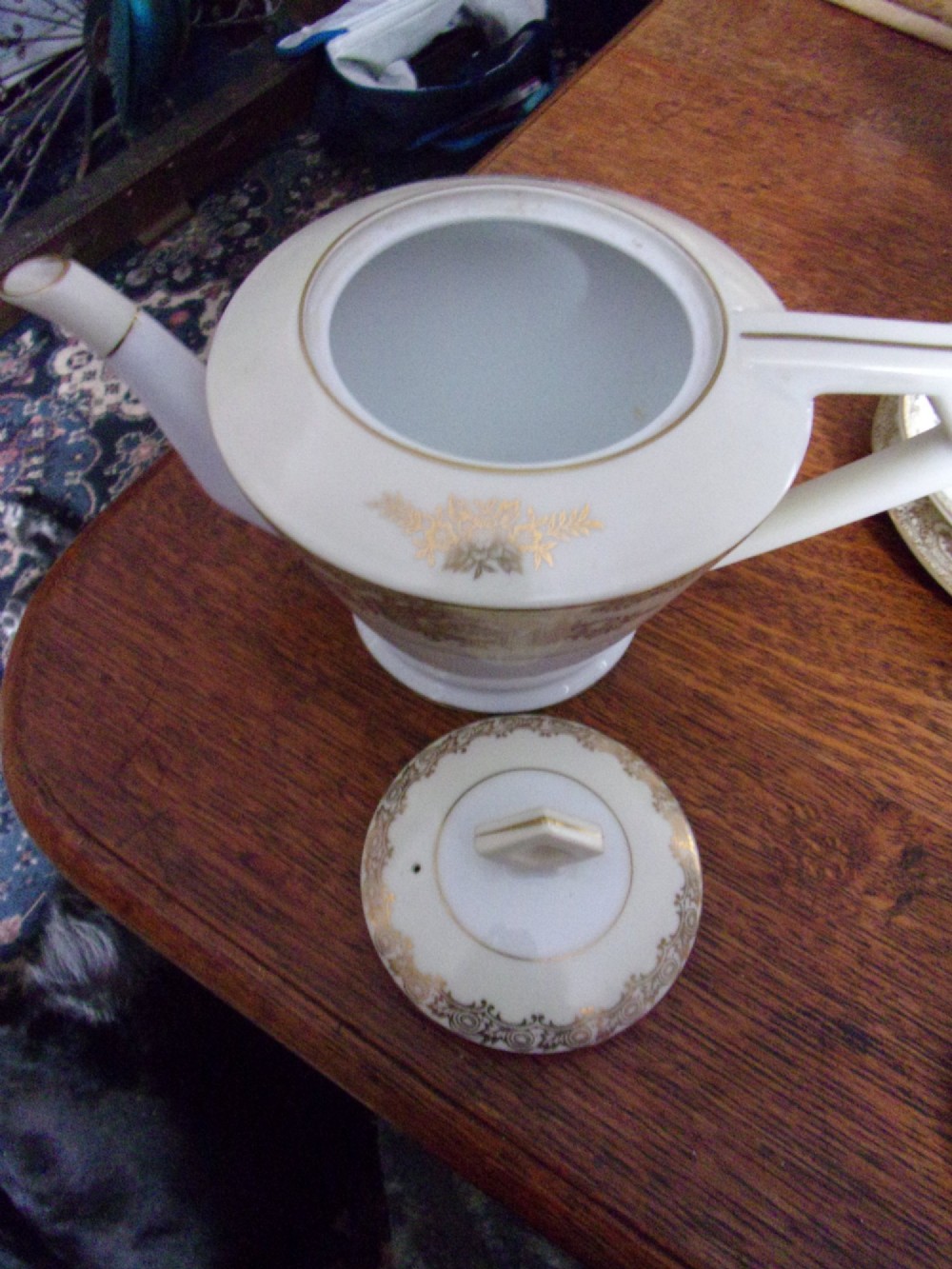 An eighteen piece cream and white porcelain tea set with gold floral gilded rims, comprising teacups, saucers, a teapot, milk pitchers, and a circular serving plate. View V