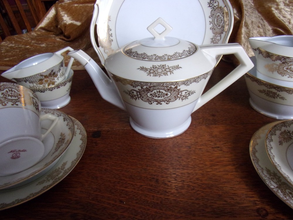 An eighteen piece cream and white porcelain tea set with gold floral gilded rims, comprising teacups, saucers, a teapot, milk pitchers, and a circular serving plate. View VI