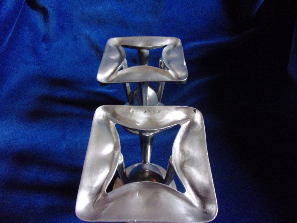 A pair of Arts and Crafts pewter candlesticks featuring square bases, four upright tapered struts, and bulbous candle sockets with flat drip rims. View III