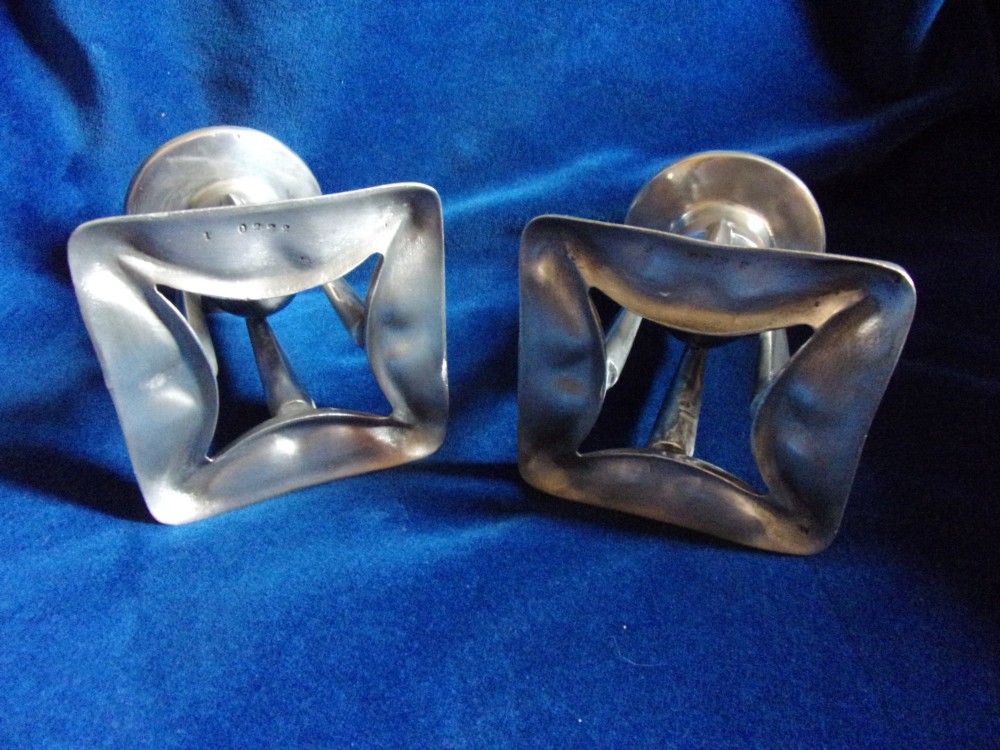 A pair of Arts and Crafts pewter candlesticks featuring square bases, four upright tapered struts, and bulbous candle sockets with flat drip rims. View IV