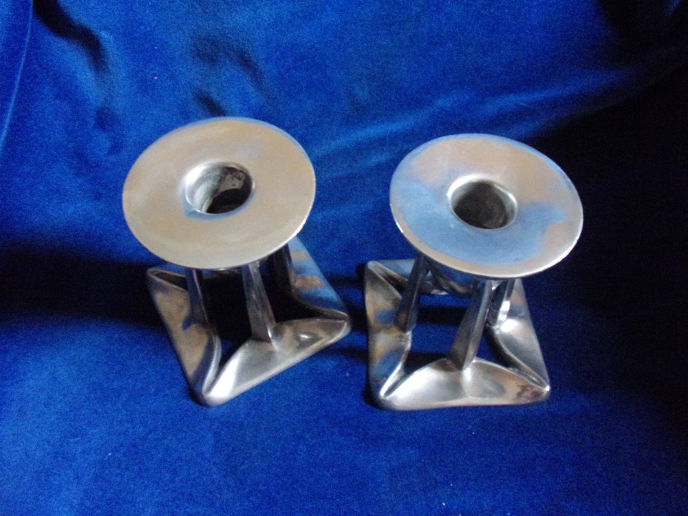 A pair of Arts and Crafts pewter candlesticks featuring square bases, four upright tapered struts, and bulbous candle sockets with flat drip rims. View V