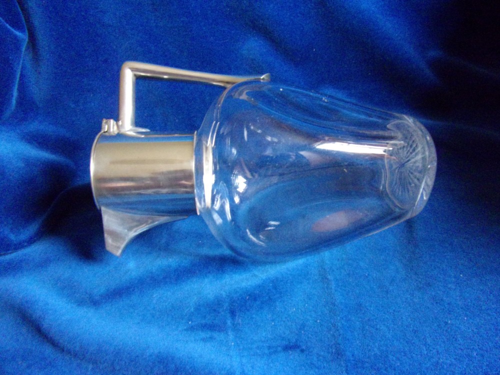 An Arts and Crafts clear glass claret jug featuring a silver-plated hinged collar, angular handle, and flat lid. View II