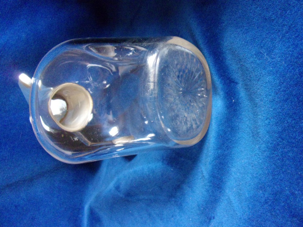An Arts and Crafts clear glass claret jug featuring a silver-plated hinged collar, angular handle, and flat lid. View V