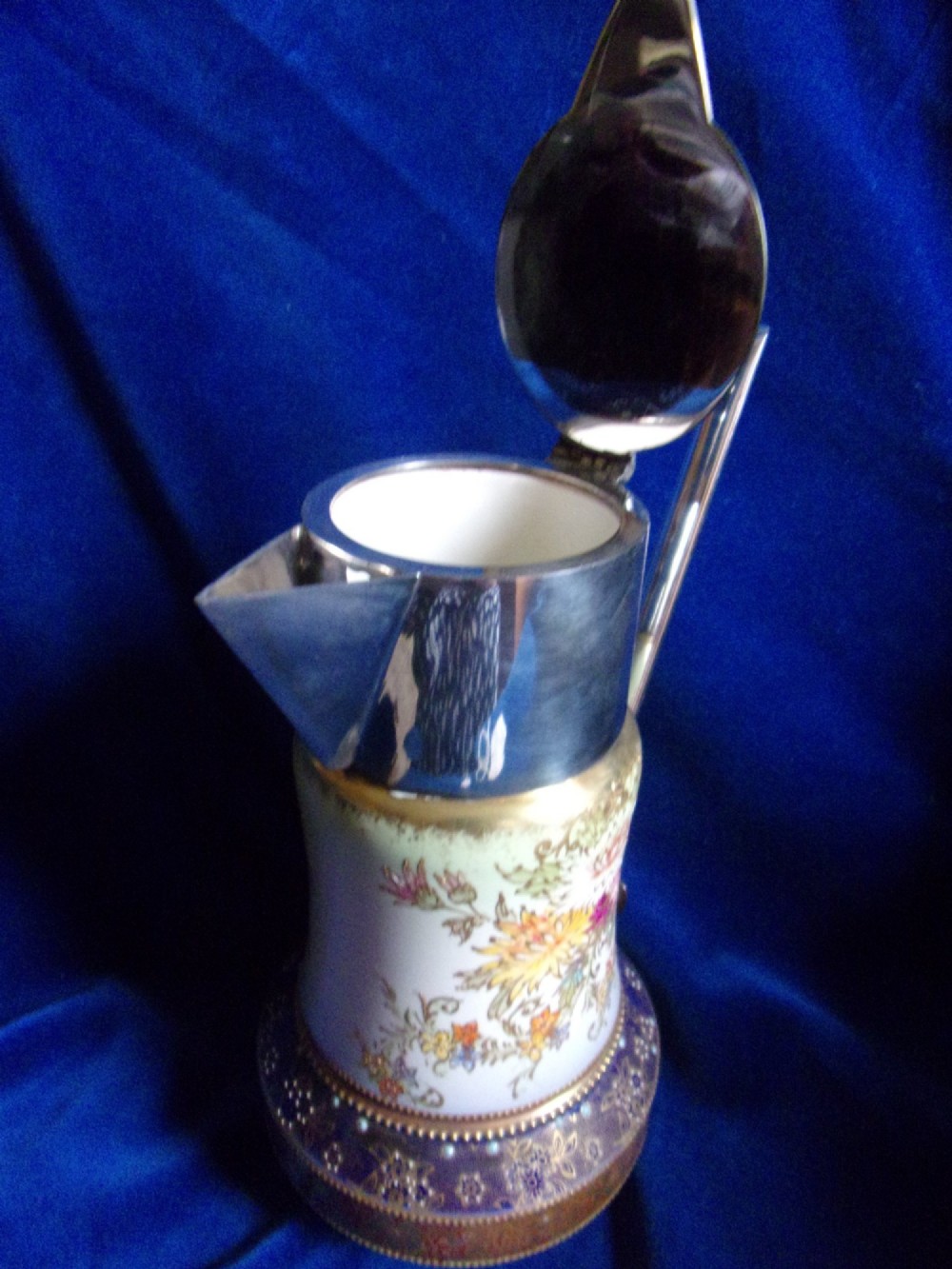 An antique Carlton Ware ceramic claret jug featuring floral enamel detailing and a polished silver-plated neck, lid, and geometric handle. View V