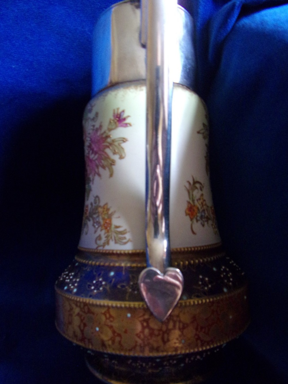 An antique Carlton Ware ceramic claret jug featuring floral enamel detailing and a polished silver-plated neck, lid, and geometric handle. View VII
