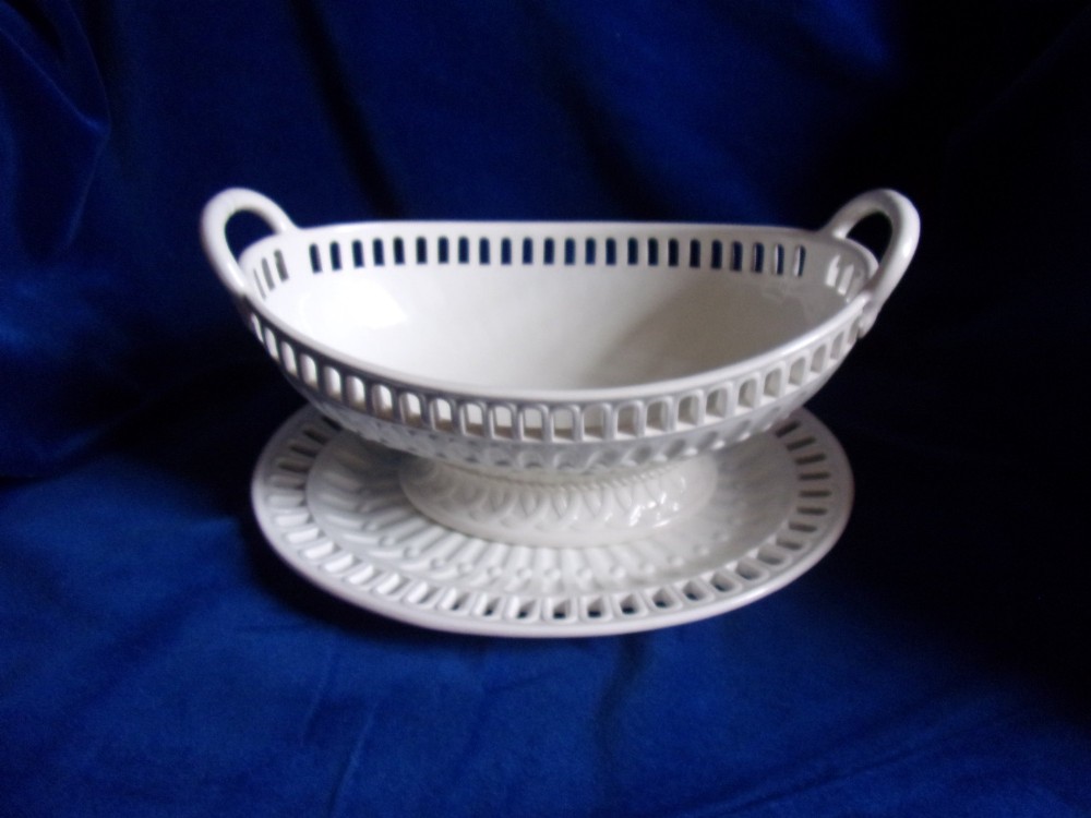 A cream-coloured glazed earthenware basket featuring pierced lattice rims, twin side handles, and a matching reticulated stand.