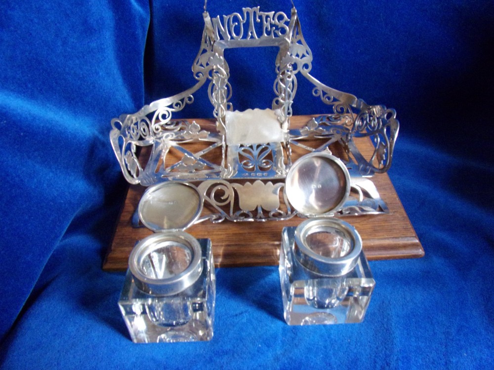 An Edwardian fretted silver standish featuring two glass inkwells mounted on a rectangular carved oak base. View II