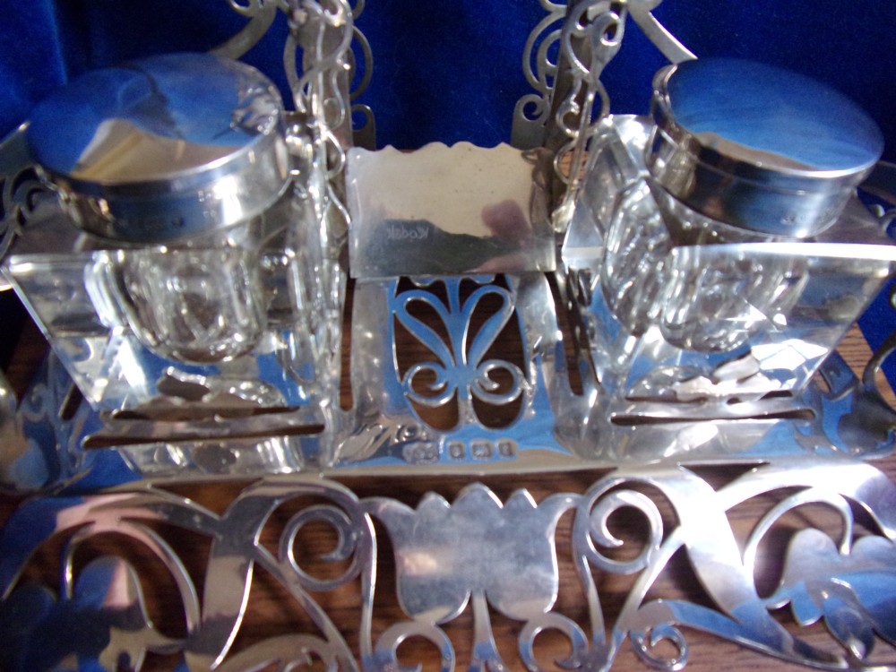 An Edwardian fretted silver standish featuring two glass inkwells mounted on a rectangular carved oak base. View IV