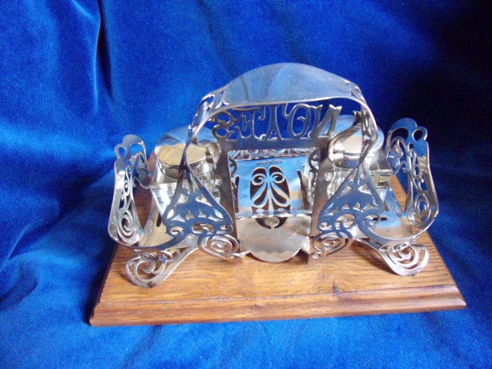 An Edwardian fretted silver standish featuring two glass inkwells mounted on a rectangular carved oak base. View VI