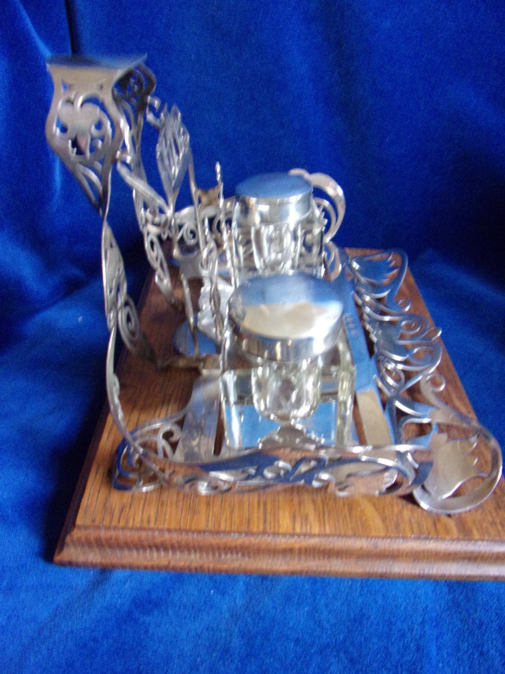 An Edwardian fretted silver standish featuring two glass inkwells mounted on a rectangular carved oak base. View V