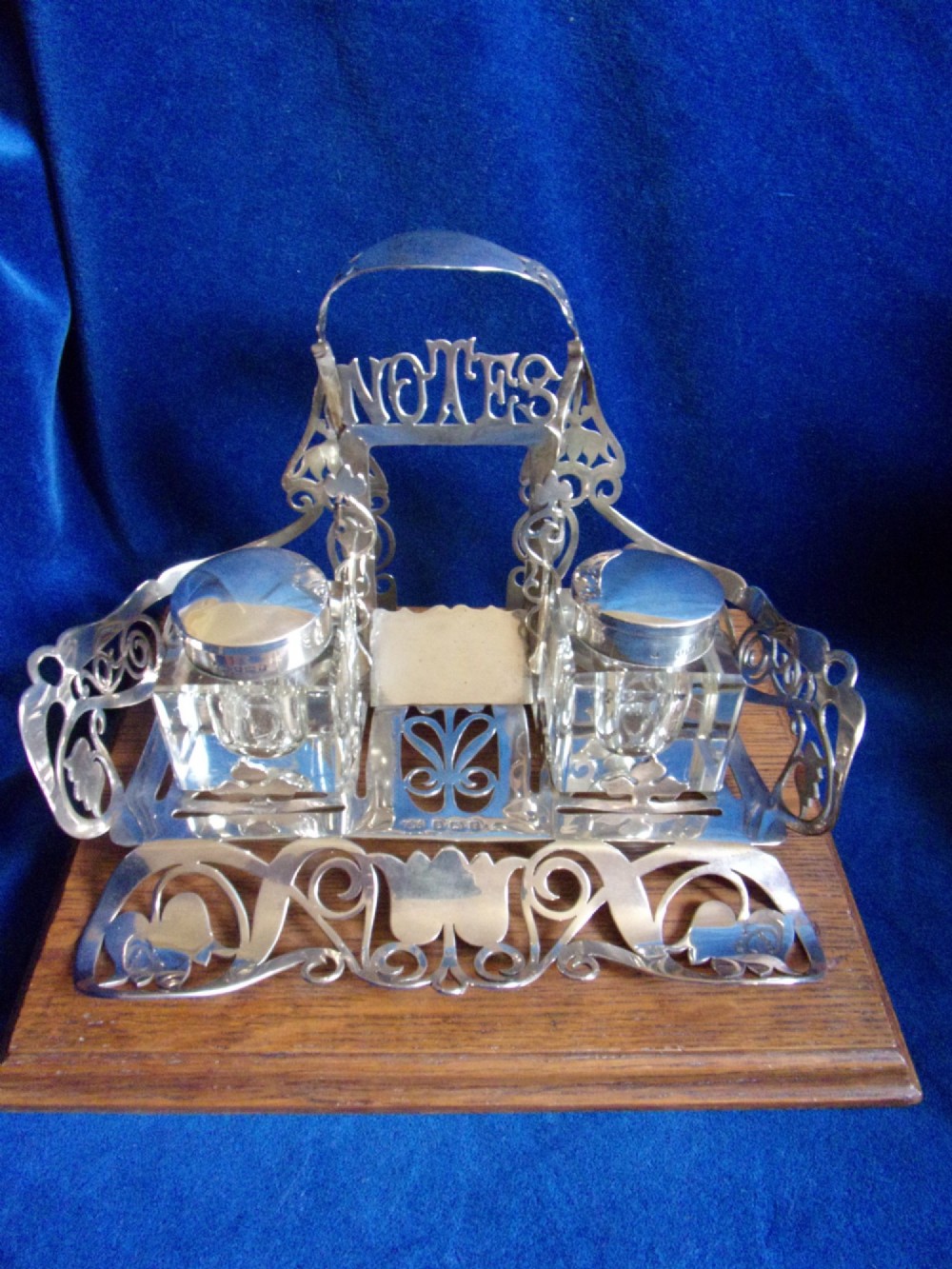 An Edwardian fretted silver standish featuring two glass inkwells mounted on a rectangular carved oak base. View IX