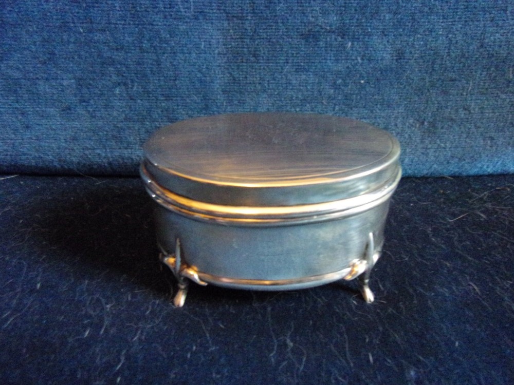 An oval sterling silver trinket box with a smooth polished lid resting on four slender cabriole feet.