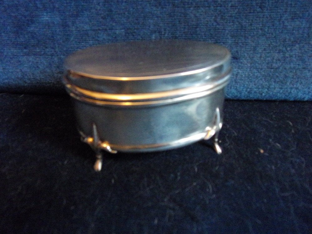 An oval sterling silver trinket box with a smooth polished lid resting on four slender cabriole feet. View III