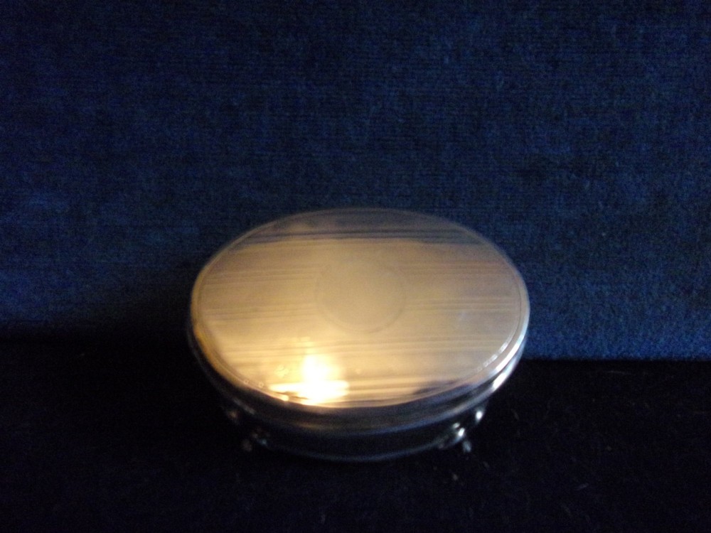An oval sterling silver trinket box with a smooth polished lid resting on four slender cabriole feet. View IV