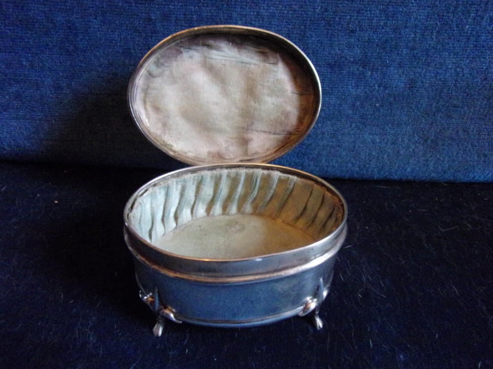 An oval sterling silver trinket box with a smooth polished lid resting on four slender cabriole feet. View V
