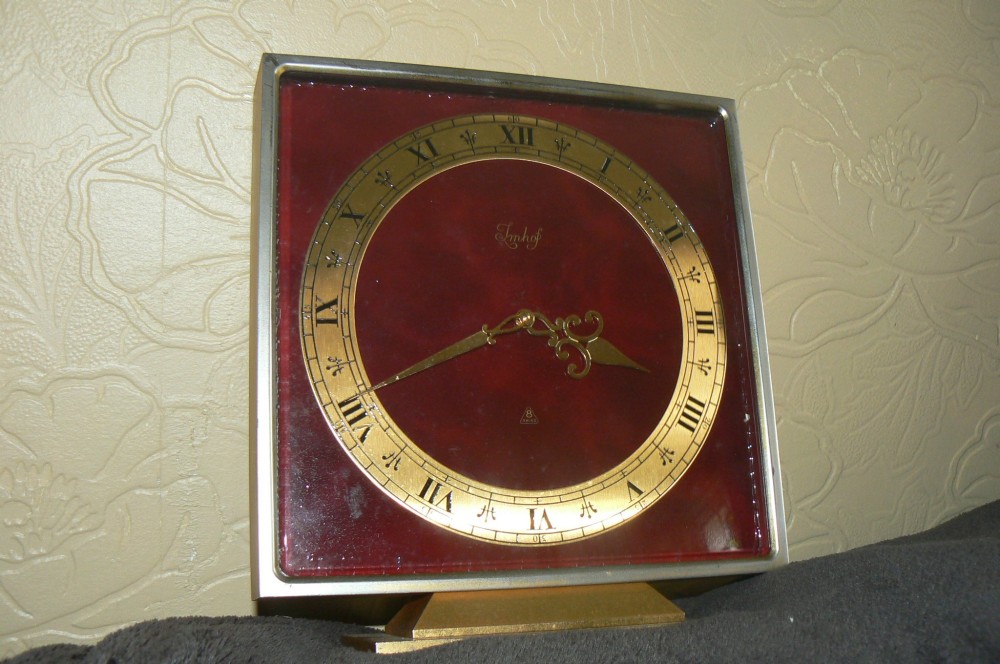 A square Art Deco style Swiss Imhof mantel clock featuring a gilt bronze frame, a dark red dial face, and a circular gold chapter ring with Roman numerals.