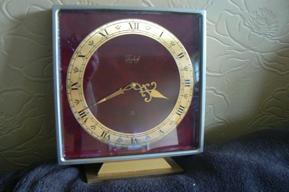 A square Art Deco style Swiss Imhof mantel clock featuring a gilt bronze frame, a dark red dial face, and a circular gold chapter ring with Roman numerals. View II