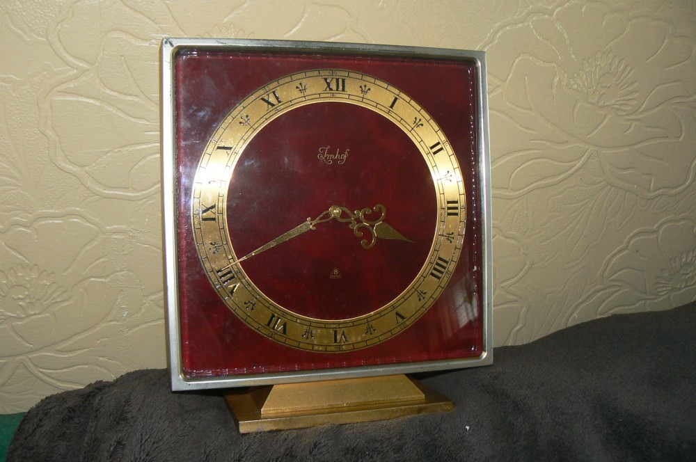 A square Art Deco style Swiss Imhof mantel clock featuring a gilt bronze frame, a dark red dial face, and a circular gold chapter ring with Roman numerals. View V