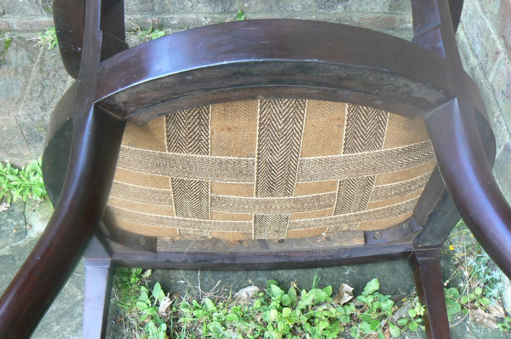 An Edwardian dark mahogany elbow chair featuring inlaid wood detail on the backrest, curved armrests, and a light beige upholstered seat. View VII