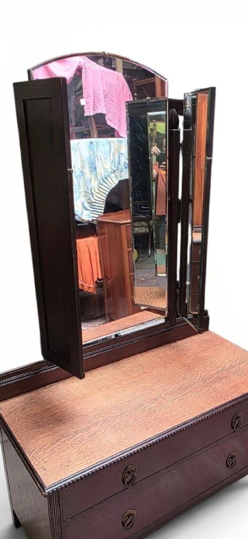 fig 2. A dark oak dressing chest featuring two wide drawers, a natural wood top surface, and an attached folding triple mirror.