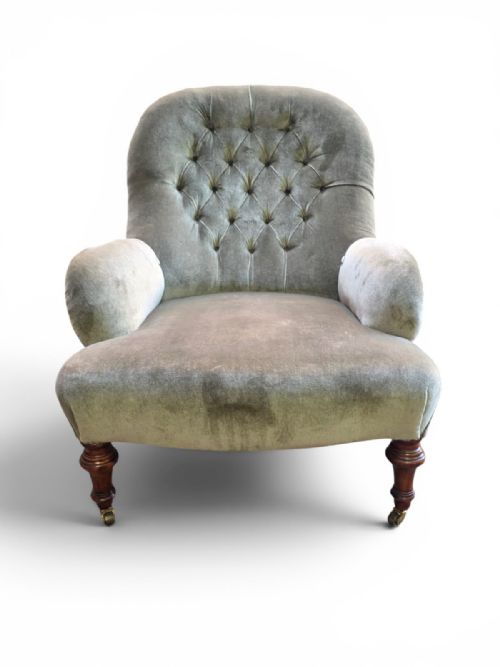 fig 1. An Edwardian button-back armchair upholstered in light sage green velvet with turned wooden front legs on brass castors.
