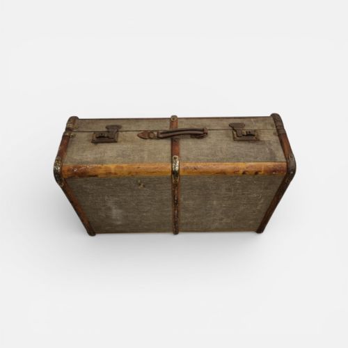 fig 1. A 1930s British Everwear travel trunk covered in grey fabric with wood banding, metal corner caps, and a central leather handle.