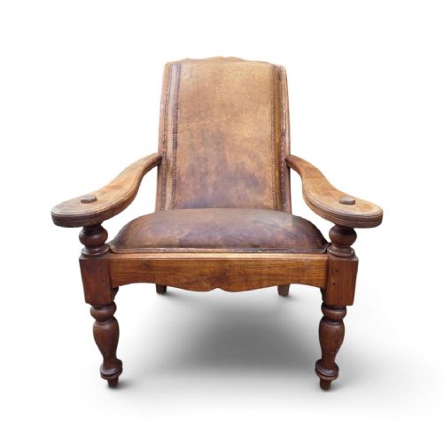 fig 1. An antique 19th-century colonial planters chair featuring a reclined tan leather seat and backrest alongside long extendable flat wooden armrests resting on turned legs.