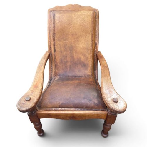 fig 2. An antique 19th-century colonial planters chair featuring a reclined tan leather seat and backrest alongside long extendable flat wooden armrests resting on turned legs.