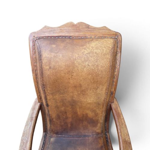fig 3. An antique 19th-century colonial planters chair featuring a reclined tan leather seat and backrest alongside long extendable flat wooden armrests resting on turned legs.