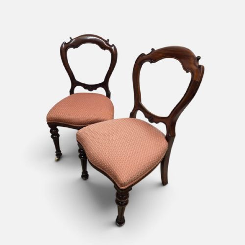fig 1. A pair of Victorian mahogany balloon back chairs with carved frames, peach patterned upholstered seats, and turned front legs on castors.