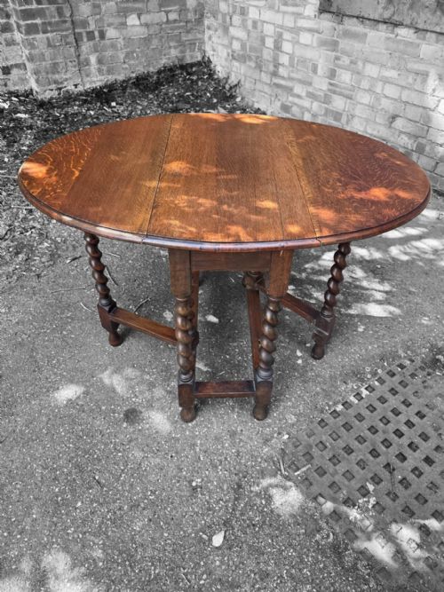fig 1. A medium brown oak drop-leaf gateleg table with barley twist legs standing folded on a paved surface.