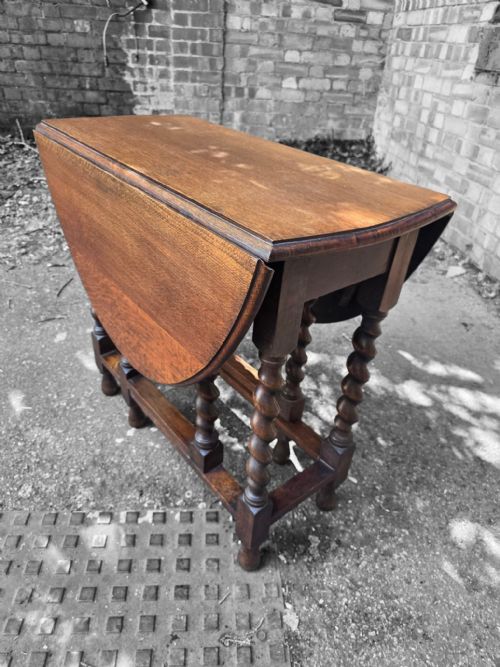 fig 2. A medium brown oak drop-leaf gateleg table with barley twist legs standing folded on a paved surface.