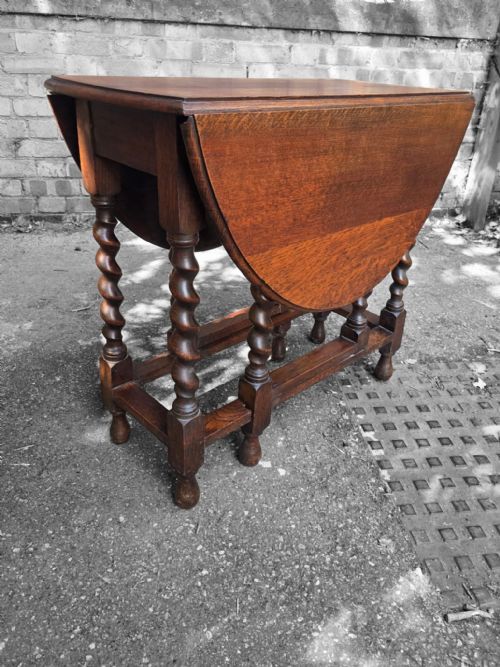 fig 3. A medium brown oak drop-leaf gateleg table with barley twist legs standing folded on a paved surface.
