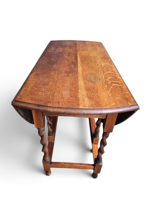 fig 1. An antique oak gateleg dining table featuring a rounded drop-leaf top supported by turned barley twist legs and lower stretchers.