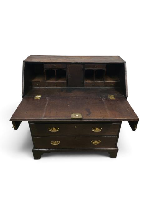 fig 1. An antique dark oak fall-front writing bureau featuring four horizontal drawers with decorative brass handles and a sloped drop-down lid.