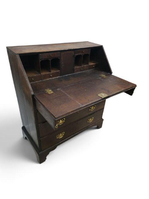 fig 2. An antique dark oak fall-front writing bureau featuring four horizontal drawers with decorative brass handles and a sloped drop-down lid.