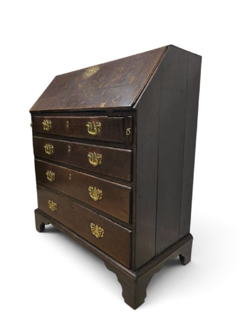 fig 3. An antique dark oak fall-front writing bureau featuring four horizontal drawers with decorative brass handles and a sloped drop-down lid.