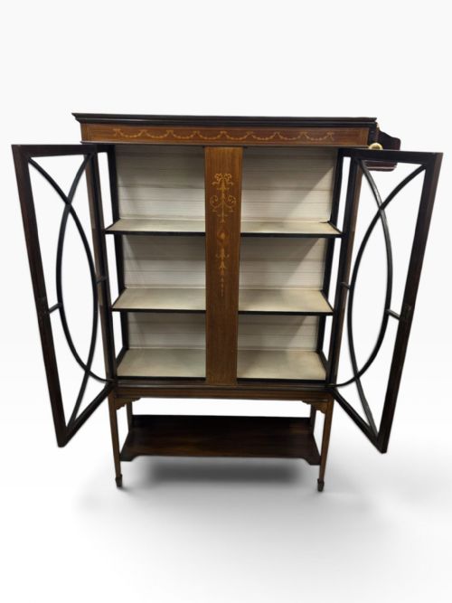 fig 1. An Edwardian mahogany display cabinet featuring inlaid marquetry details, astragal glazed twin doors, and an open lower undertier shelf.