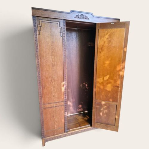 fig 1. An antique 1920s Art Deco oak wardrobe featuring a central mirrored door, geometric inlay detailing, and carved accents.