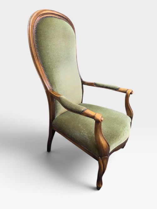 fig 1. An antique Victorian high back armchair featuring a polished timber frame, olive green velvet upholstery, and brass stud trim.