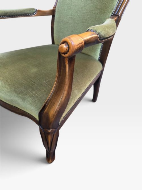 fig 3. An antique Victorian high back armchair featuring a polished timber frame, olive green velvet upholstery, and brass stud trim.