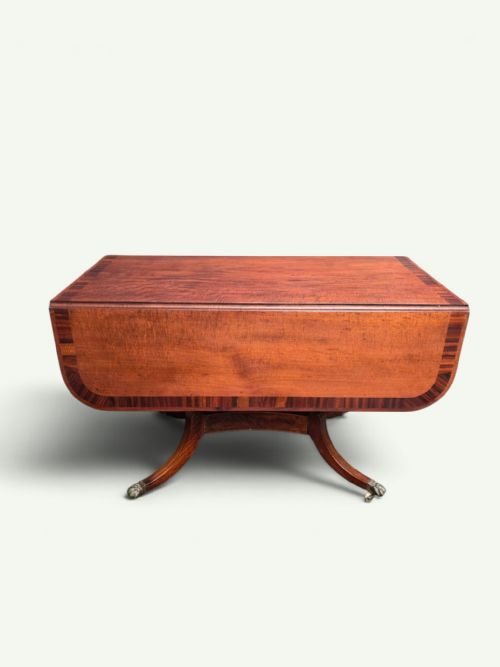 fig 1. A Regency mahogany Pembroke drop-leaf table with crossbanded inlay, a pedestal base on splayed legs, and brass claw feet with castors.