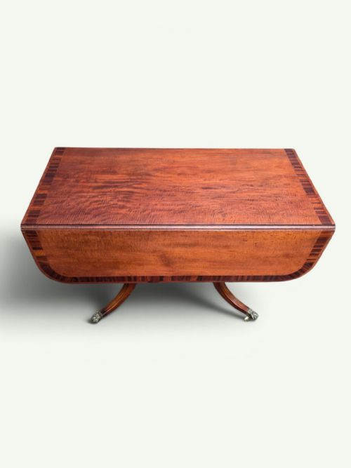 fig 2. A Regency mahogany Pembroke drop-leaf table with crossbanded inlay, a pedestal base on splayed legs, and brass claw feet with castors.