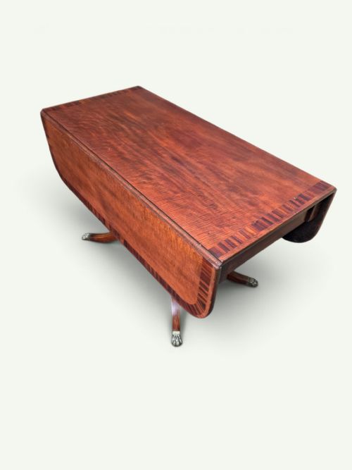 fig 3. A Regency mahogany Pembroke drop-leaf table with crossbanded inlay, a pedestal base on splayed legs, and brass claw feet with castors.