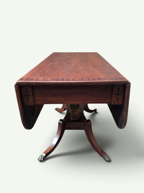 fig 4. A Regency mahogany Pembroke drop-leaf table with crossbanded inlay, a pedestal base on splayed legs, and brass claw feet with castors.