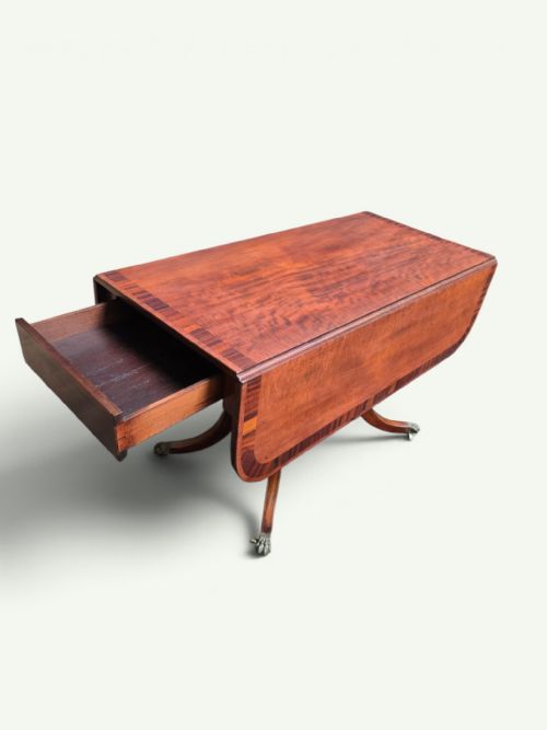 fig 5. A Regency mahogany Pembroke drop-leaf table with crossbanded inlay, a pedestal base on splayed legs, and brass claw feet with castors.