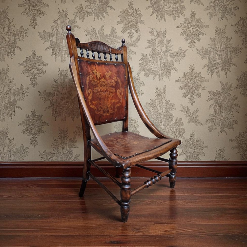 An Edwardian beech occasional chair featuring floral marquetry on the backrest and seat, turned front legs, and decorative brass studs.