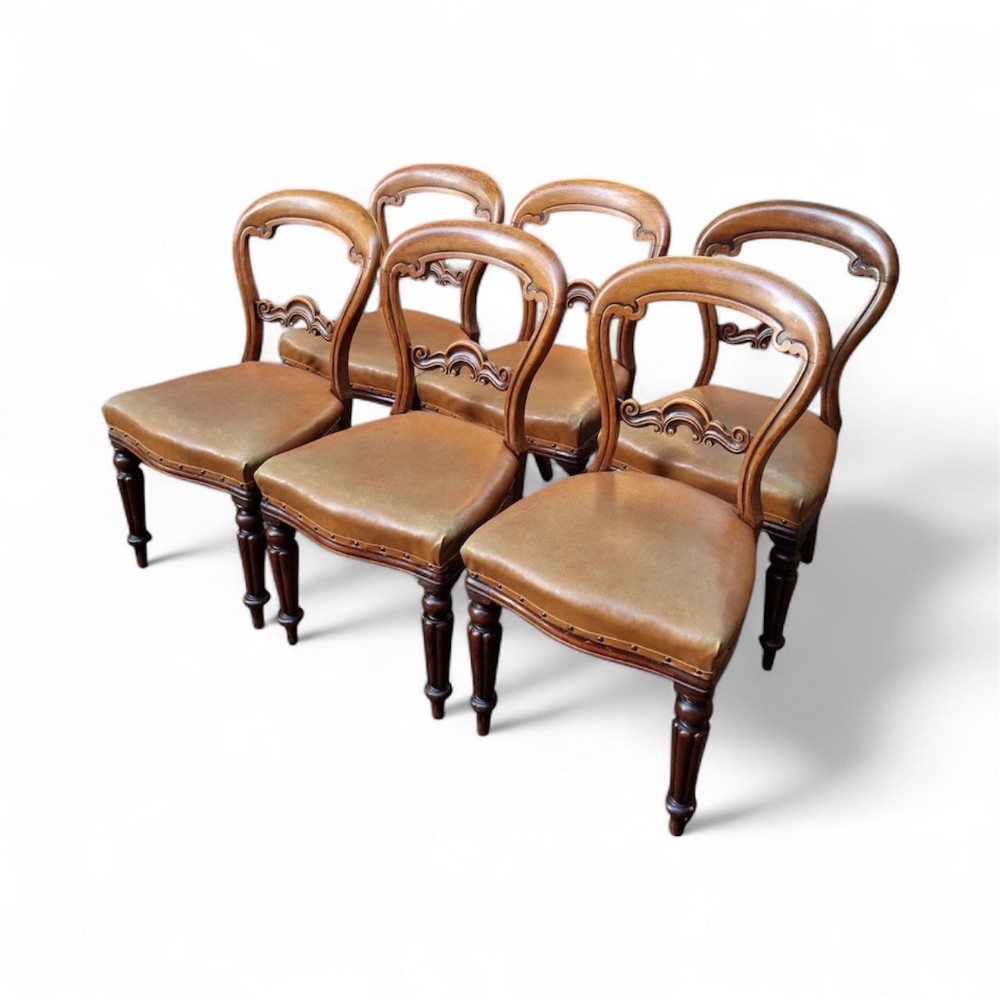 Set of six Victorian balloon back dining chairs featuring carved timber frames, turned front legs, and brown leather seats.