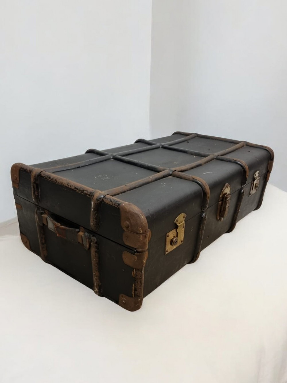 A rectangular black travel trunk featuring dark wooden reinforcement bands, brass latches, and reinforced metal corner caps.