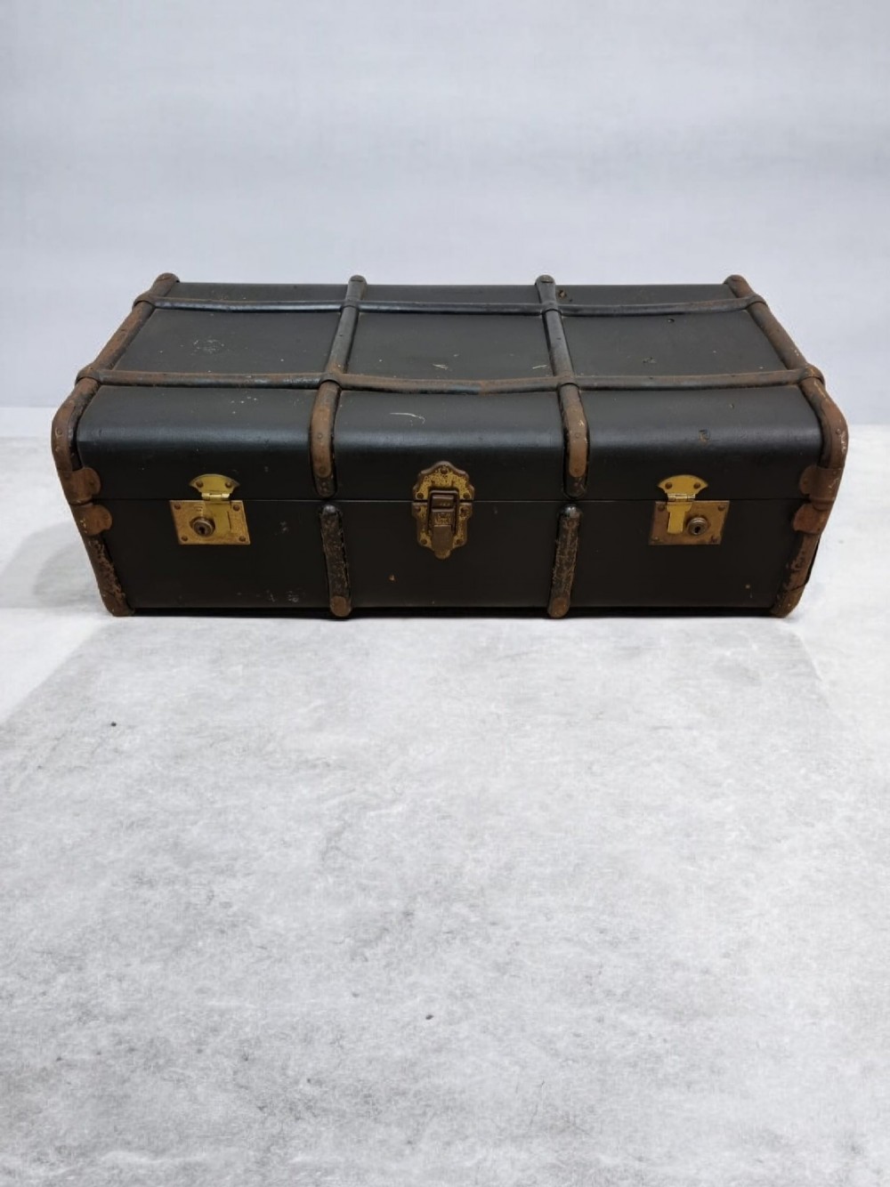 A rectangular black travel trunk featuring dark wooden reinforcement bands, brass latches, and reinforced metal corner caps. View VII